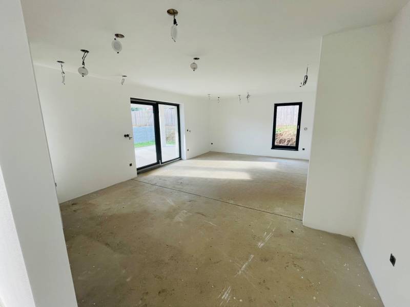 Interior of a family house with a concrete floor and large windows providing a view of the garden.