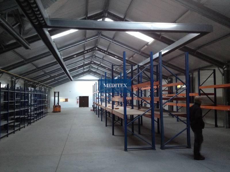 There are empty shelves in the warehouse and a person is standing by them.