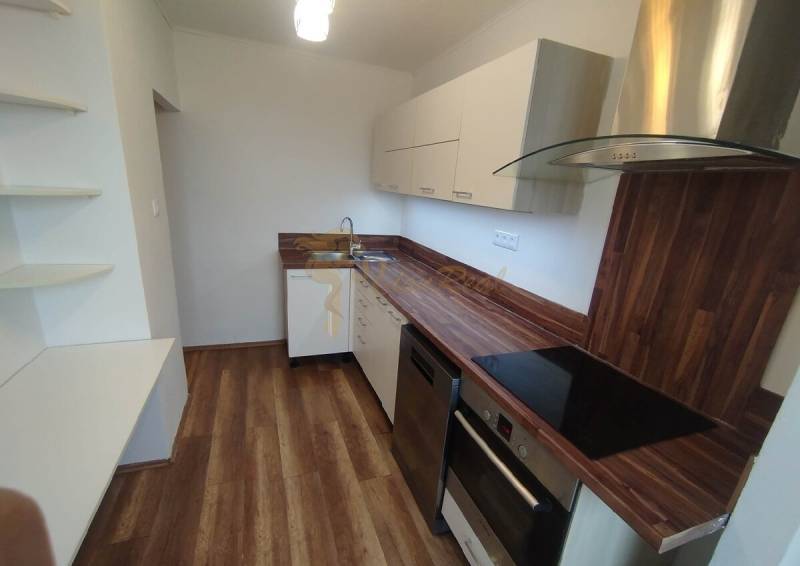 A kitchen unit with a wooden countertop in a 3-room apartment, white cabinets, and built-in appliances.