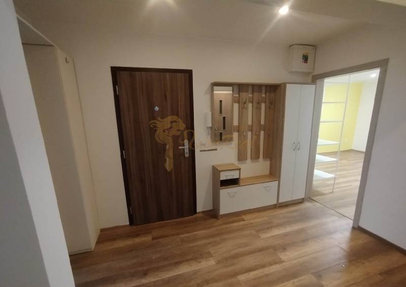 A hallway in a 3-room apartment with a wooden floor and a coat rack wall.