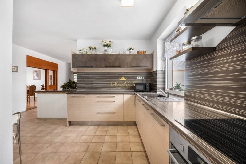 A family house kitchen with wooden cabinets, a dining area, and a window.