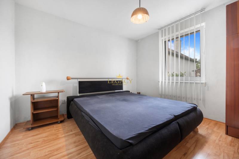 A bedroom in a family house with wooden floors, a dark bed, and a nightstand.