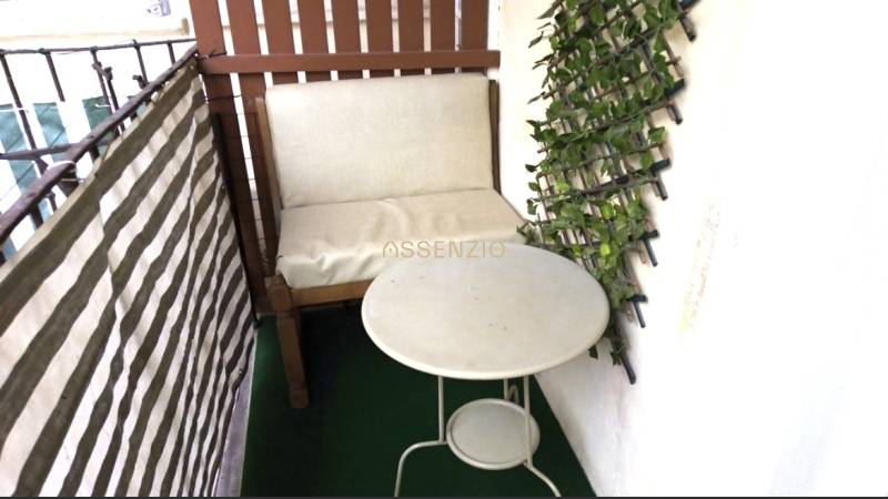 A balcony in a 3-room apartment with a chair, table, and vertical greenery on the wall.
