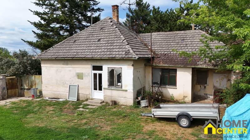 Older family house in Kolárovo with an extension, garden, and a trailer in front of the house.