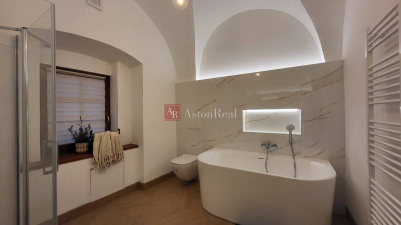A bathroom with a freestanding bathtub in a 2-room apartment with a lighted shelf.