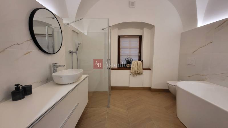 A bathroom in a 2-room apartment with a sink, shower, bathtub, and window.