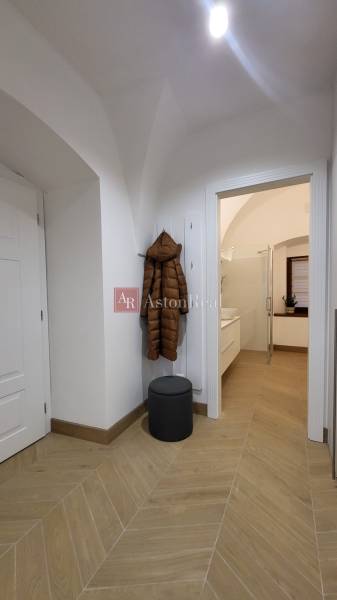 The hallway in a 2-room apartment with a wooden floor, a coat on the hanger, and open doors to the bathroom.