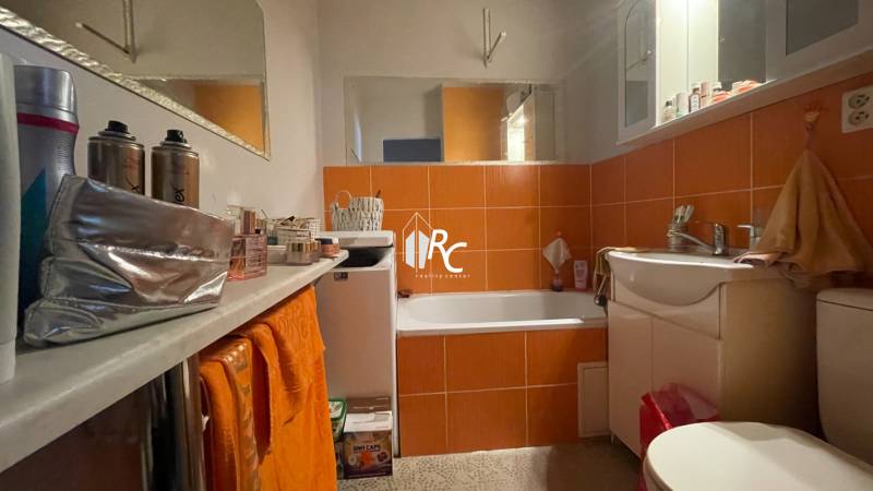 A bathroom with white furniture and orange tiles in a studio apartment.