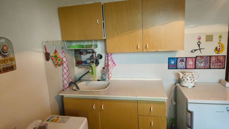 A kitchen in a studio apartment with a sink, a kettle, and decorations on the wall.