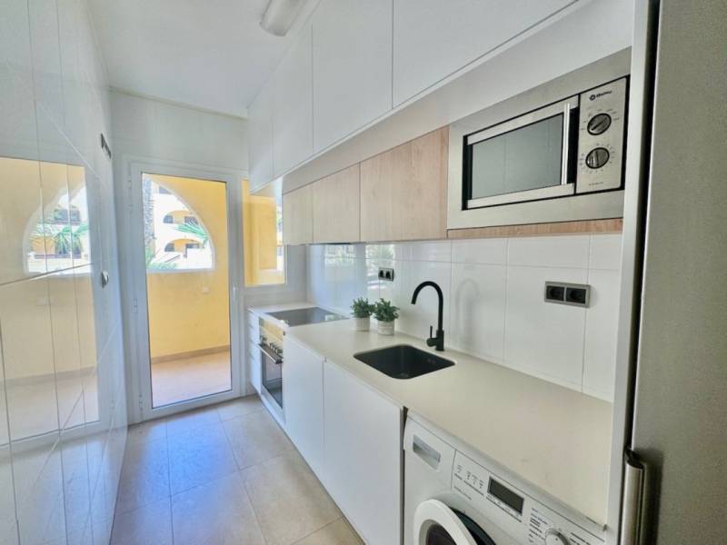 The kitchen in the vacation apartment, equipped with appliances, a sink, and white cabinets, with access to the balcony.