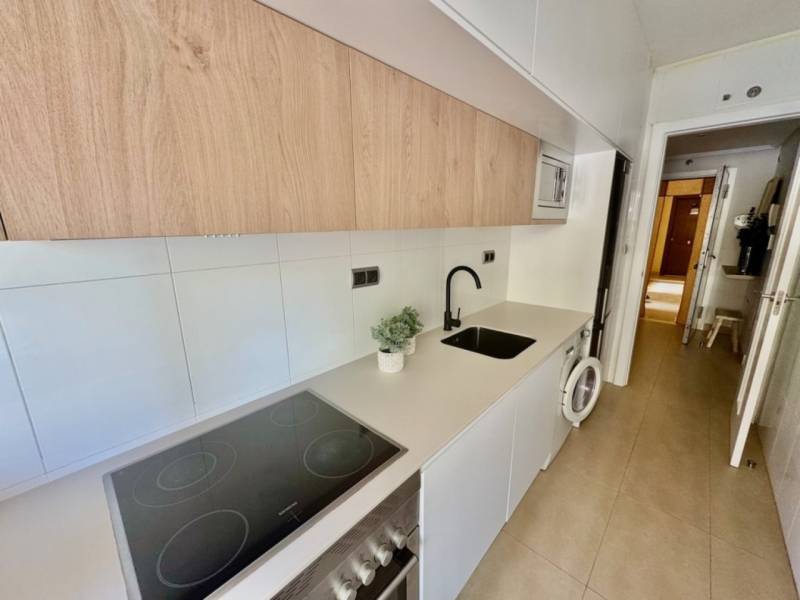 A narrow kitchen with a cooktop, washing machine, and wood-paneled cabinets in a vacation apartment.