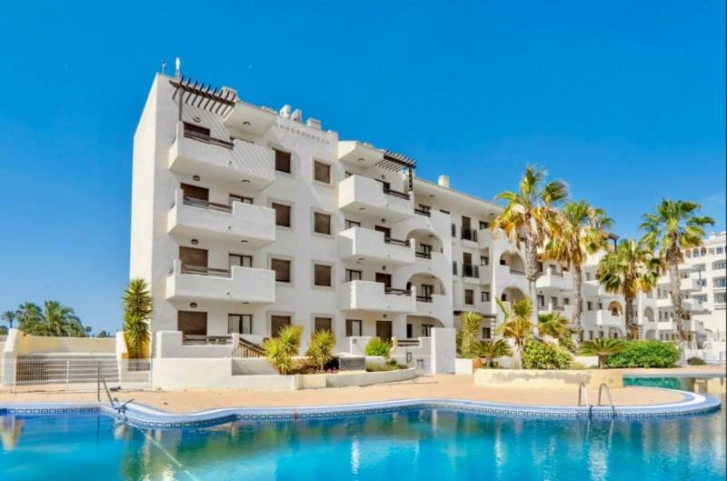 Recreational apartment in Los Alcázares with a pool, palm trees, and blue sky.