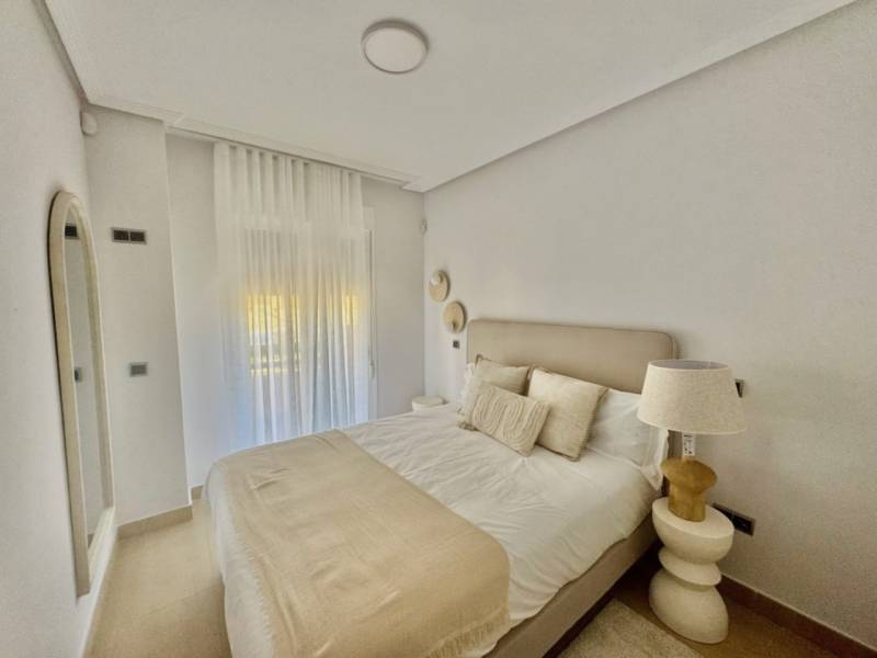A bedroom in a holiday apartment with a comfortable bed, a mirror, and curtains.