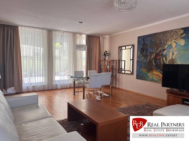 Living room with wooden flooring and a sofa in a three-room apartment, large windows with delicate curtains.