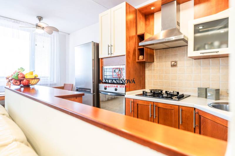 A kitchen in a 3-room apartment with wooden cabinets and a stove, illuminated by natural light.
