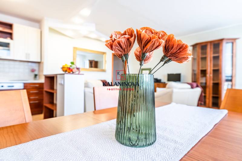 A vase with flowers on the table in a 3-room apartment with a kitchen in the background.