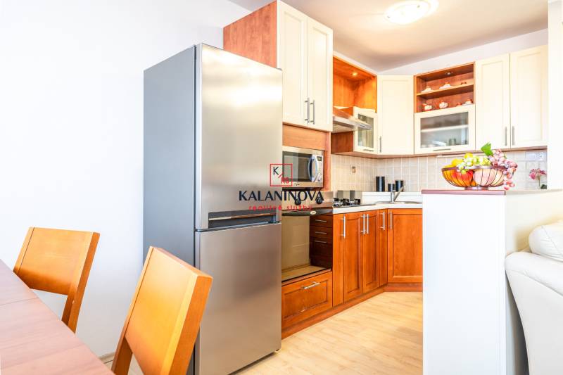 A kitchen in a 3-room apartment with wooden cabinets, a refrigerator, and a fruit bowl on the table.