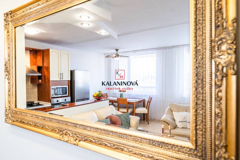 The kitchen and living room of a 3-room apartment captured in a mirror with a gold frame.