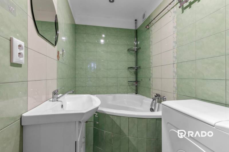 A bathroom in a 3-room apartment with a corner bathtub and green tiles.