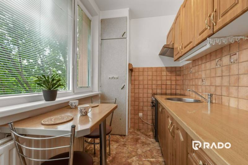 The kitchen of a three-room apartment with a wooden cabinet and a large window with internal blinds.