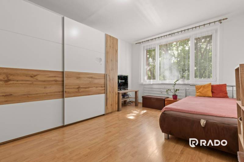 A bedroom with a built-in wardrobe, a sofa, and a window in a three-room apartment.