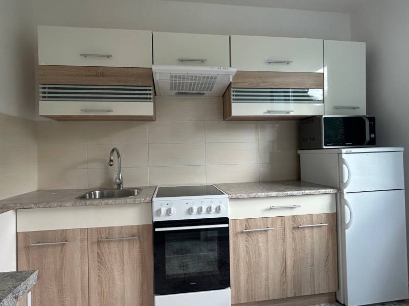 A kitchen with wooden cabinets, a stove, and a microwave in a studio apartment.
