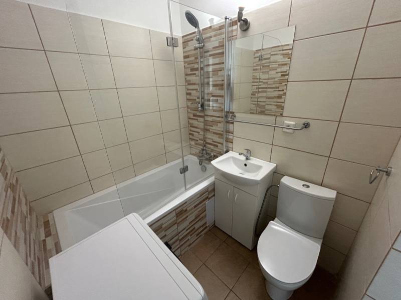 Bathroom in a studio apartment with a bathtub, sink, washing machine, and toilet.