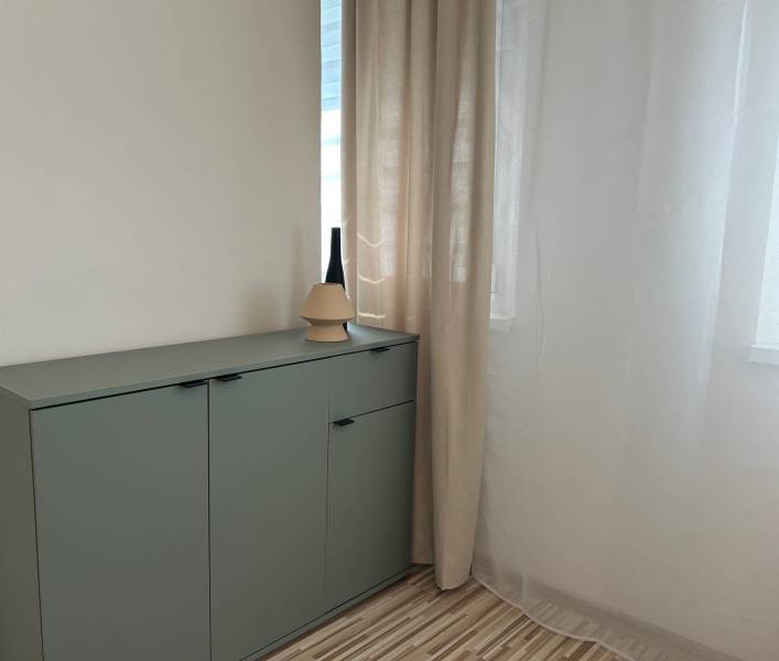 A green cabinet with decoration in a studio apartment by a white curtain and wall.