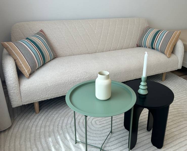 A white sofa with striped cushions, a green and black table in a studio apartment.