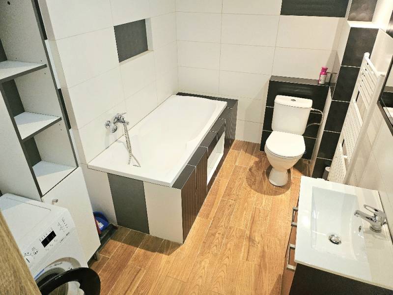 Bathroom of a 2-room apartment with a bathtub, sink, toilet, and washing machine.