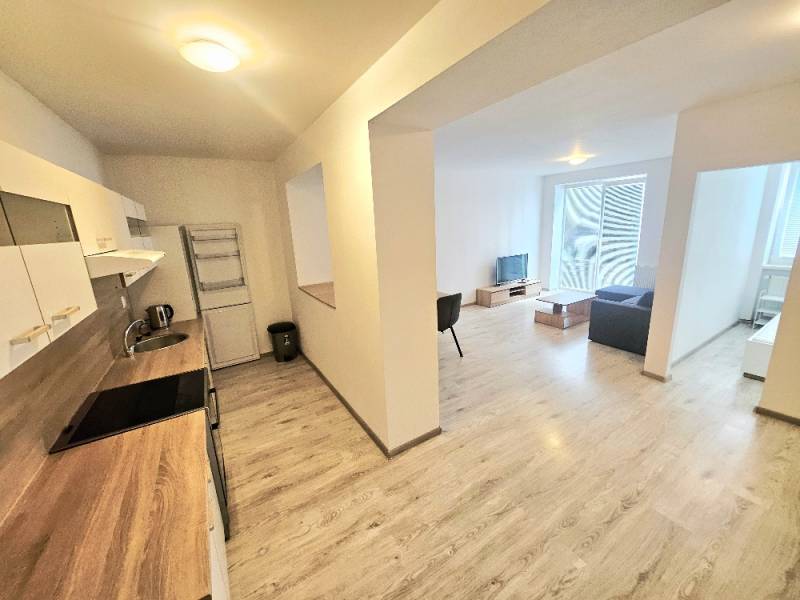 A kitchen connected to the living room in a 2-room apartment, light floors, minimalist furniture.