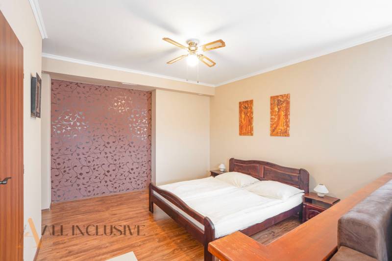 A bedroom with a wooden bed, a fan, and decorative paintings in hotels and guesthouses.