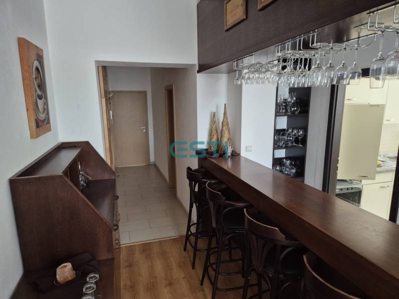 A bar counter with stools in a studio apartment, next to a hallway with wooden doors.