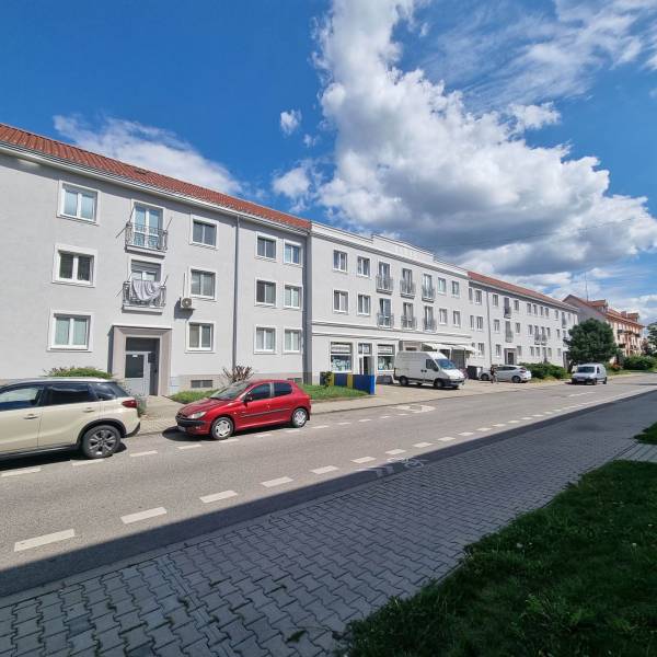 1st May Street in Malacky with parking in front of three-story buildings, visible cars and sidewalk.