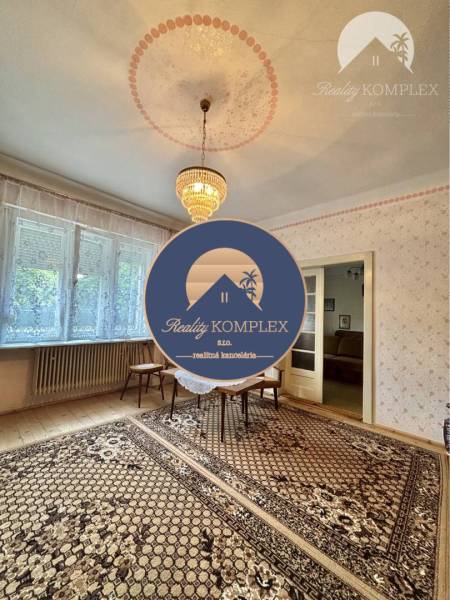 A room in a family house with a chandelier, carved floor, carpet, and a large window.