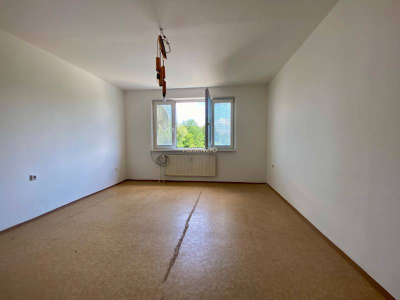 An empty room in a 3-room apartment with a window and a radiator on the wall.