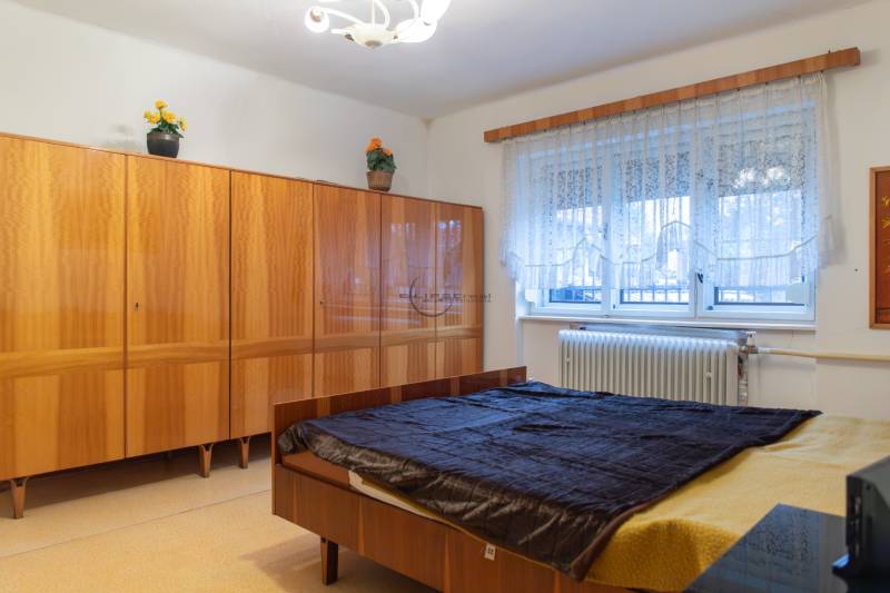 A bedroom in a family house with a bed, a wooden wardrobe, and a window with a radiator.