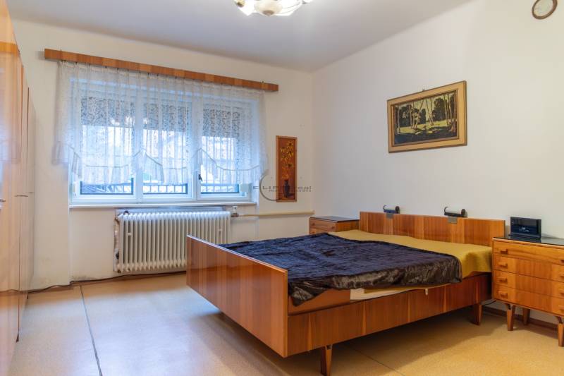 Bedroom of a family house with a wooden bed, a row of wardrobes, and a large window.