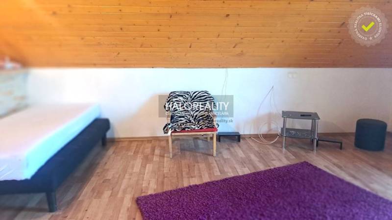 Attic room in a cottage with a bed, chair, purple carpet, and wooden paneling.