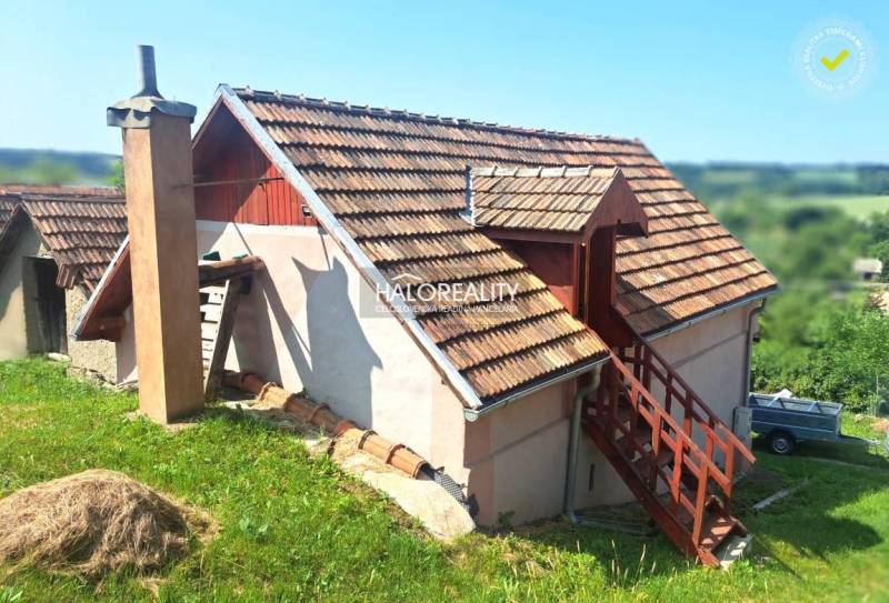 A cottage in Hontianske Trsťany with a wooden roof and an external staircase surrounded by nature.