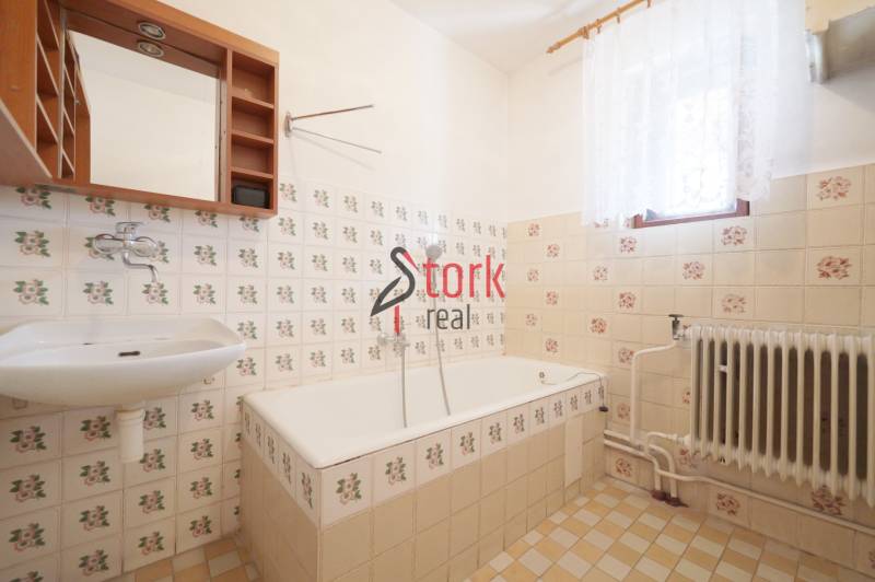 A bathroom in a family house with retro tiles and a bathtub, decorative flooring, and a radiator.