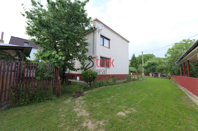 A family house in Dolná Mariková surrounded by a garden and a wooden fence on a grassy area.