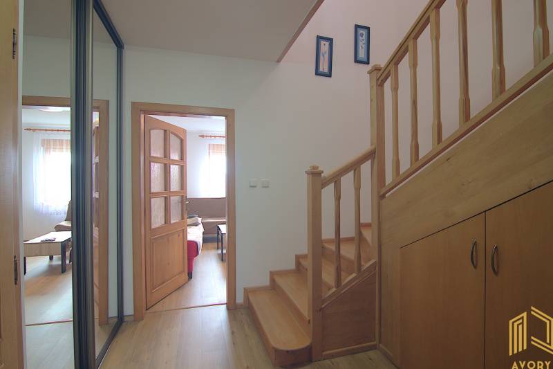Interior of a family house with a wooden staircase, entrance to the living room, and storage space.