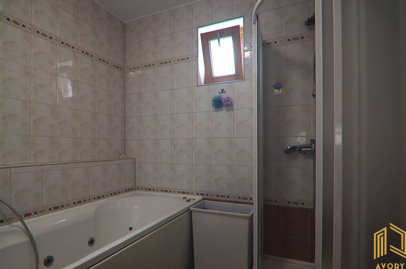 A bathroom in a family house with tiles, a bathtub, and a shower corner.