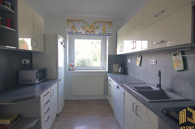 A kitchen in a family house with white cabinets, a large window, and appliances.