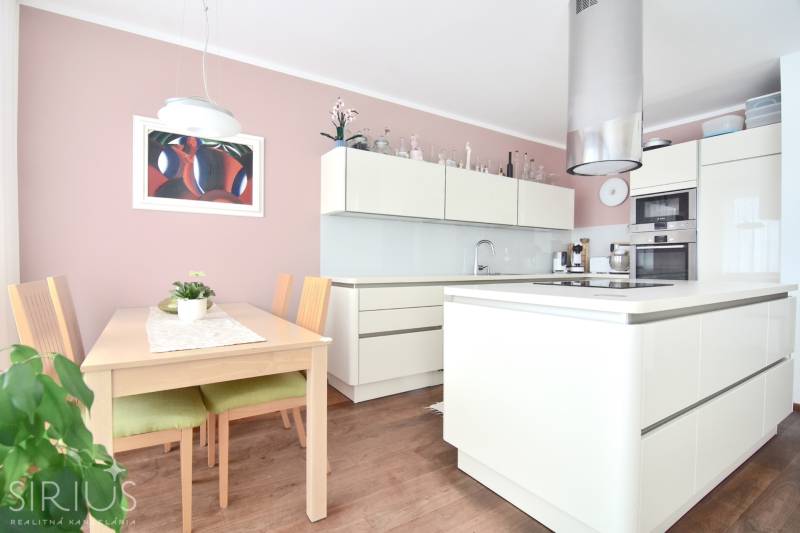 A kitchen in a 4-room apartment with a pink wall, a wooden table, and a modern kitchen unit.