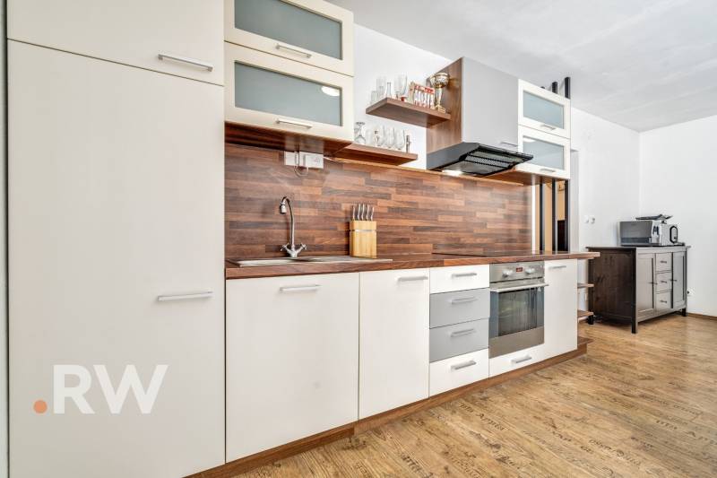 A kitchen in a 3-room apartment with wooden flooring and white and brown cabinets.
