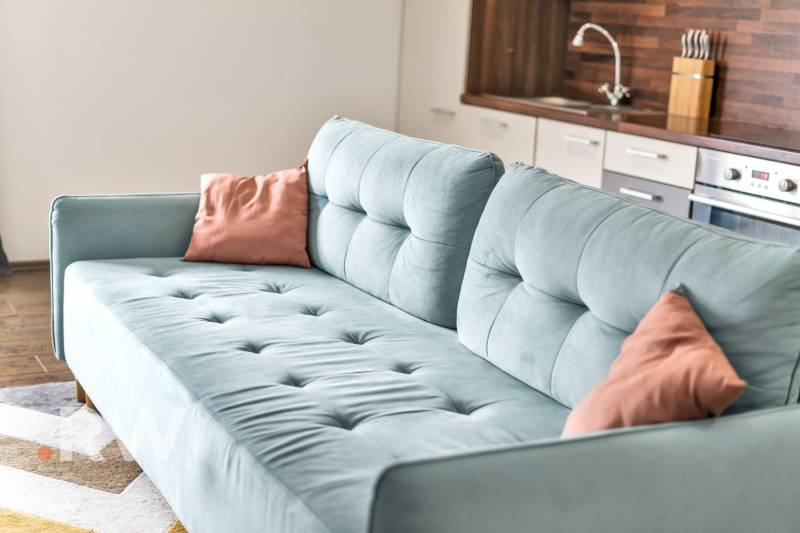 Light blue sofa and kitchen in a 3-room apartment with wooden flooring.
