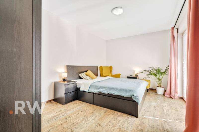 A bedroom in a 3-room apartment with a bed, nightstands, and a comfortable armchair.