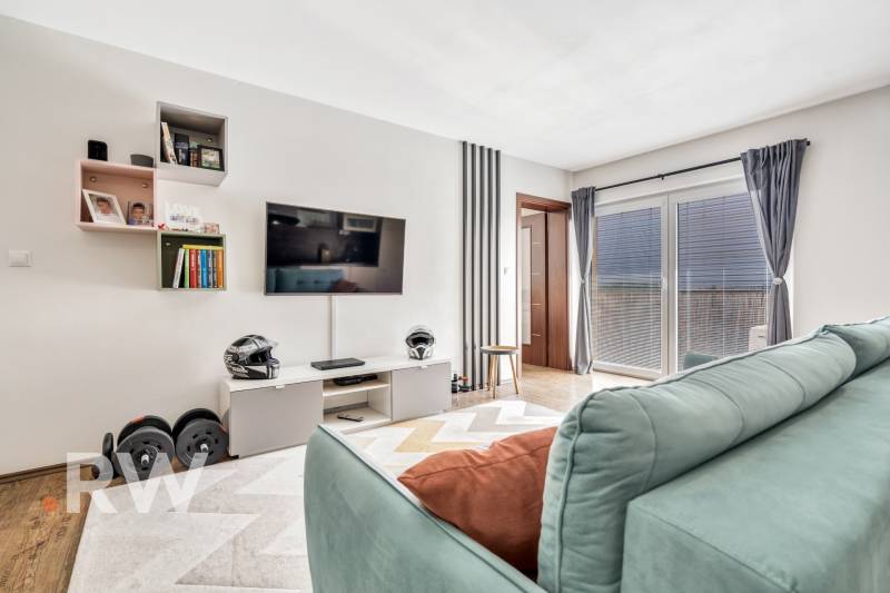 Living room in a 3-room apartment with a television, shelves, a couch, and large windows.